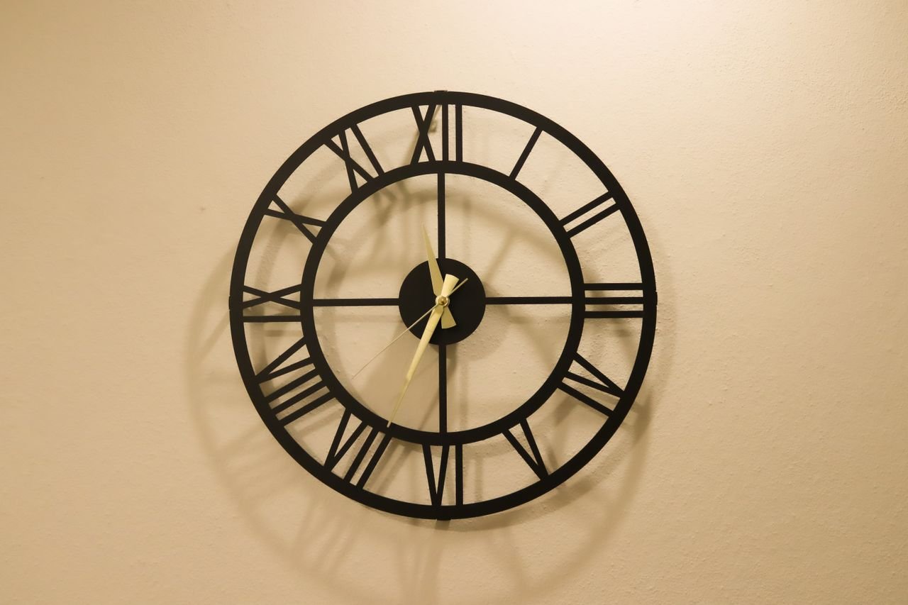 Decorative black metal wall clock with Roman numerals on a beige wall, creating a classic look.